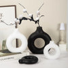 A display of white and black ceramic-look vases and a branch of roses on a light surface.