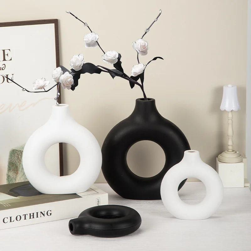 A display of white and black ceramic-look vases and a branch of roses on a light surface.
