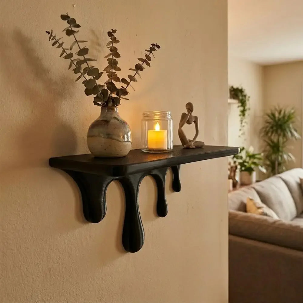 A dark floating shelf holds a vase with greenery and a glowing candle, alongside a small wooden sculpture on a light-colored 