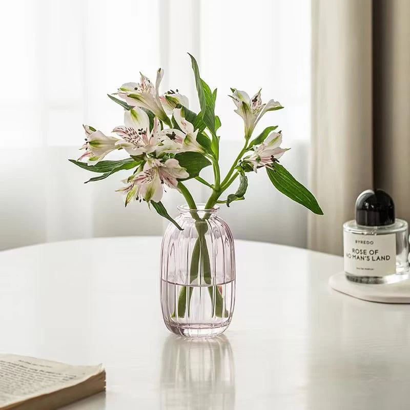 A clear glass vase holds a bouquet of white and green flowers on a white table.