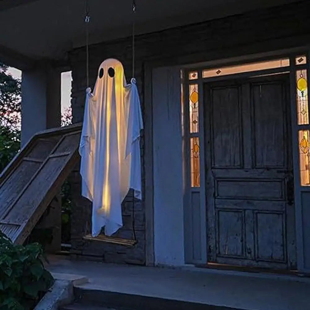 A white ghost decoration with an LED light hangs on a wooden door in the evening.