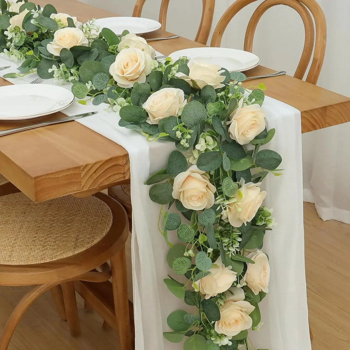 Lange Girlande aus künstlichen Rosen und Eukalyptusgrün auf einer Tischdekoration.