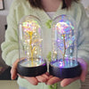 Une main tient une rose de verre éternelle avec une lumière LED pour la décoration intérieure, brillant vivement.