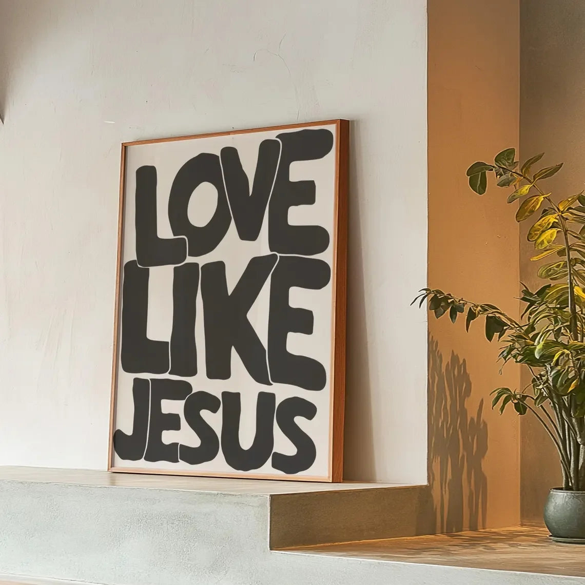 Black text on a white background reads Love Like Jesus framed in wood on a light gray ledge.