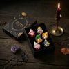 A collection of Halloween witch mini dwarf resin figurines in various colors displayed on a dark wooden surface with a lit ca