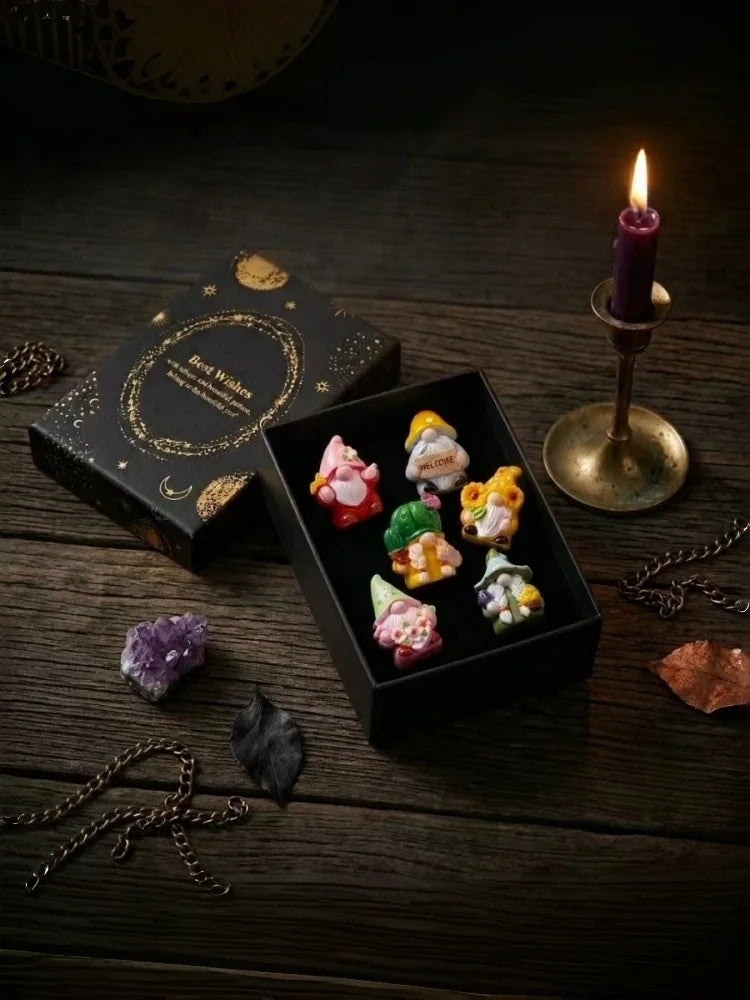 A collection of Halloween witch mini dwarf resin figurines in various colors displayed on a dark wooden surface with a lit ca
