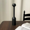 A black, vintage wooden candle holder with a flared top and cylindrical base sits on a dark wooden table.