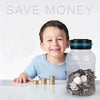 A smiling boy is sitting at a table with coins in front of a clear glass jar and a digital coin counting piggy bank.
