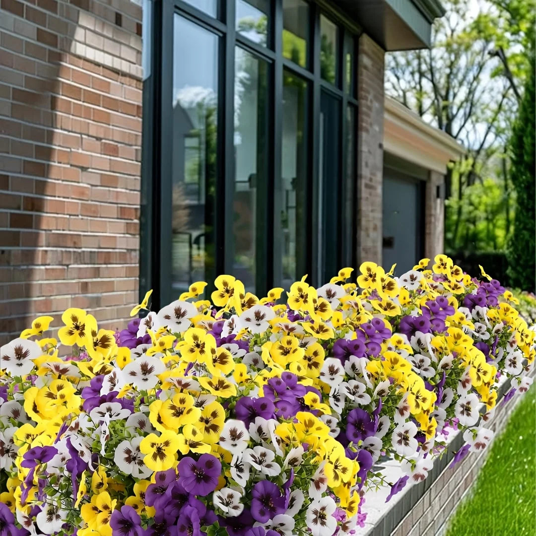 A vibrant border of artificial pansy flowers in yellow, purple, and white lining a brick walkway.