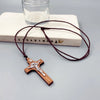 A wooden cross necklace with a wax rope cord resting on a light-colored book and clear glass.