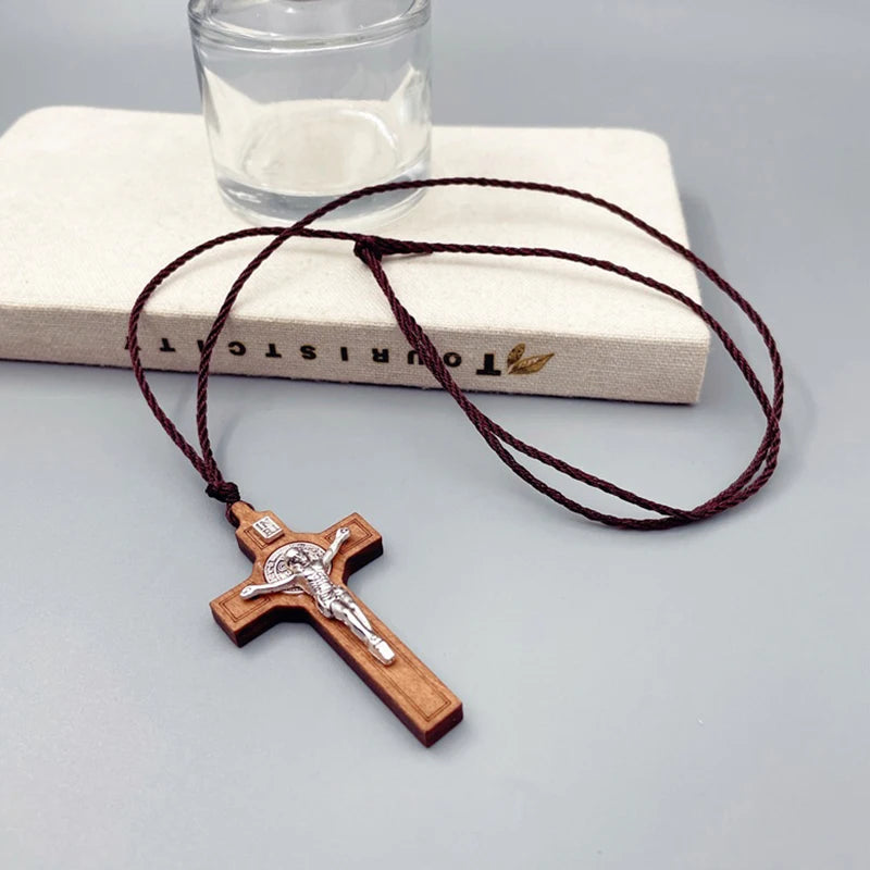 A wooden cross necklace with a wax rope cord resting on a light-colored book and clear glass.