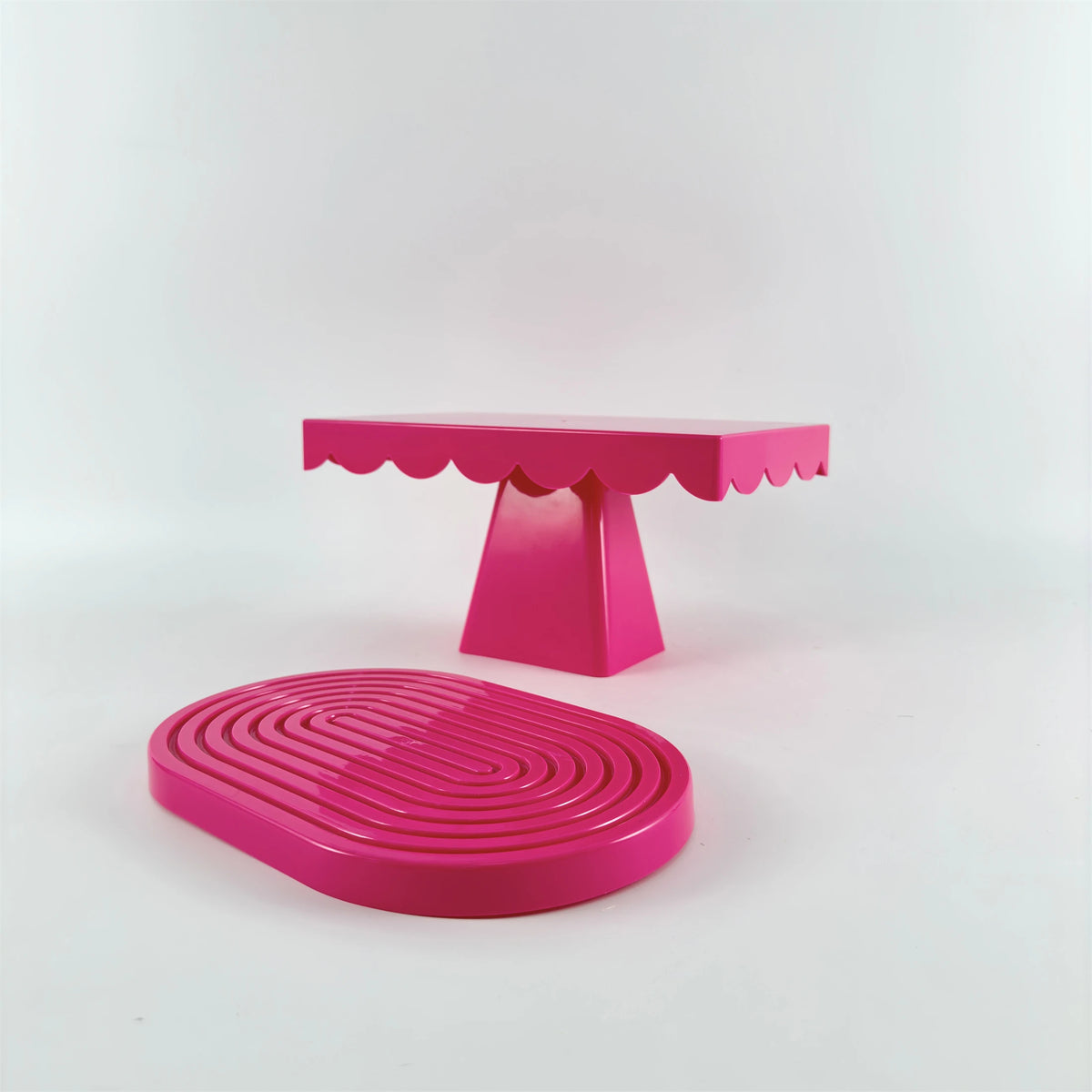 A pink cupcake stand with a ruffled top and a pink circular cake stand on a white background.