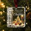 Clear acrylic ornament featuring a Christmas tree, gifts, and text on a velvet ribbon against a green pine branch background.