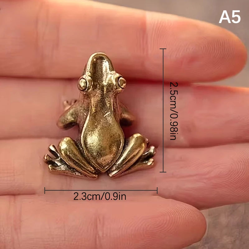 A vintage brass frog statue ornament is shown resting on a person's fingers.