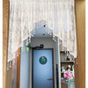 A sheer white beaded lace valance curtain hangs over a doorway, featuring delicate fringe details.