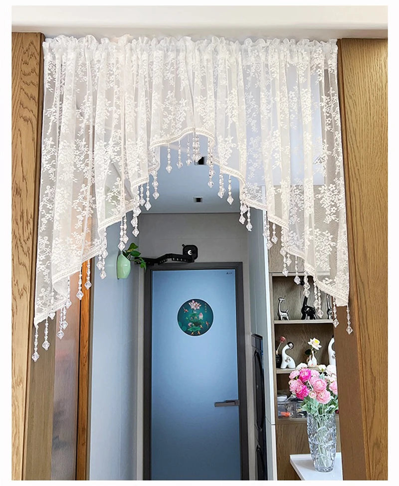 A sheer white beaded lace valance curtain hangs over a doorway, featuring delicate fringe details.