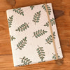 A cream linen photo album with a green leafy pattern lies on a wooden surface.