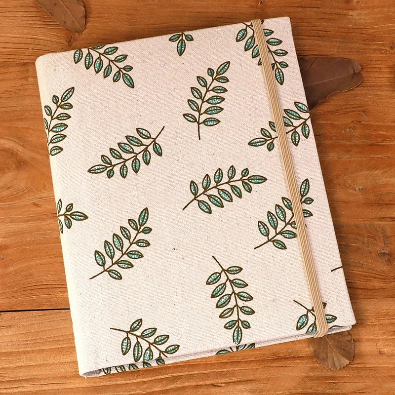 A cream linen photo album with a green leafy pattern lies on a wooden surface.