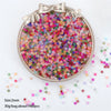 A silver-rimmed round container filled with multi-colored frosted glass rice beads for jewelry making