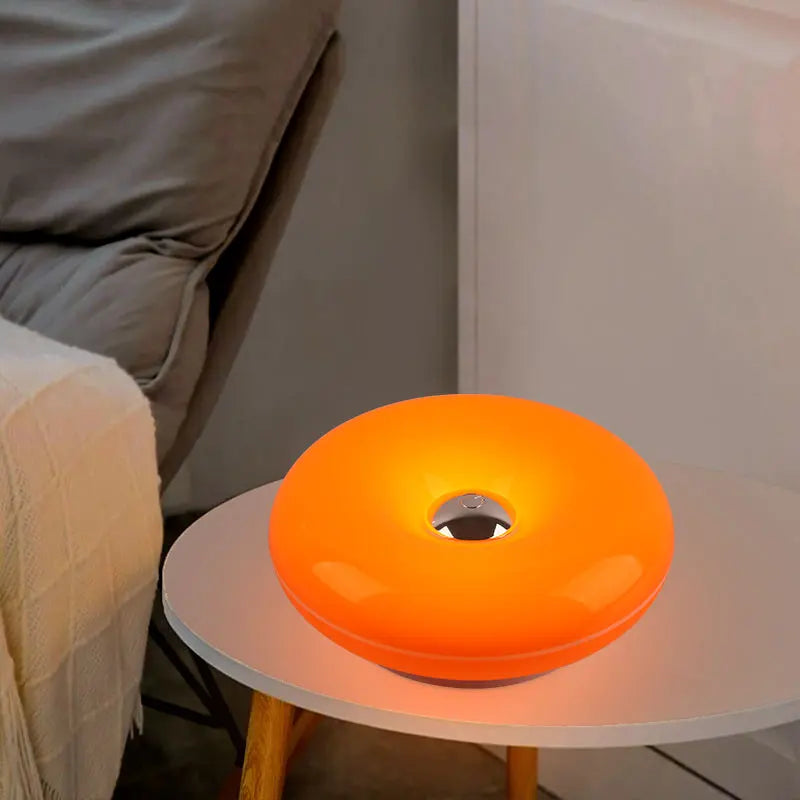 Orange, donutförmige, wiederaufladbare Wandlampe auf einem weißen Tisch.