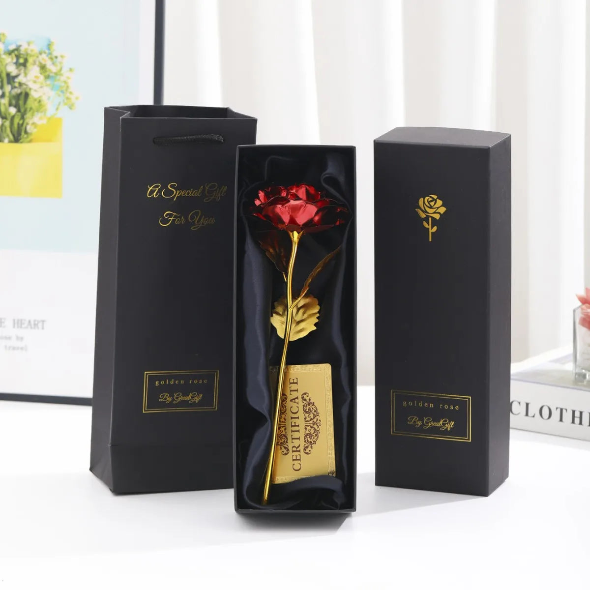 Three black gift boxes with gold foil accents and a red rose inside, presented on a white surface.