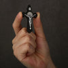 A hand holds a black wooden crucifix pendant featuring the image of Jesus Christ.