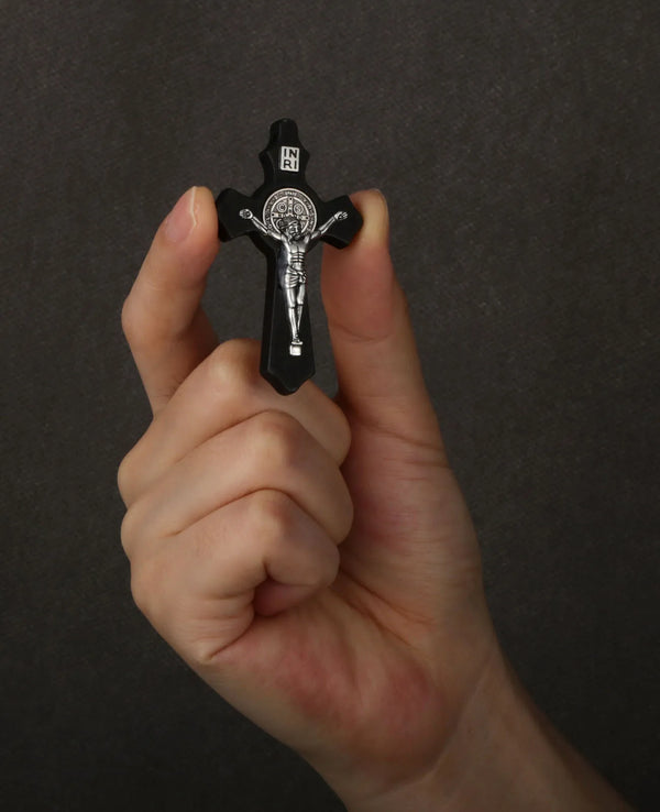 A hand holds a black wooden crucifix pendant featuring the image of Jesus Christ.