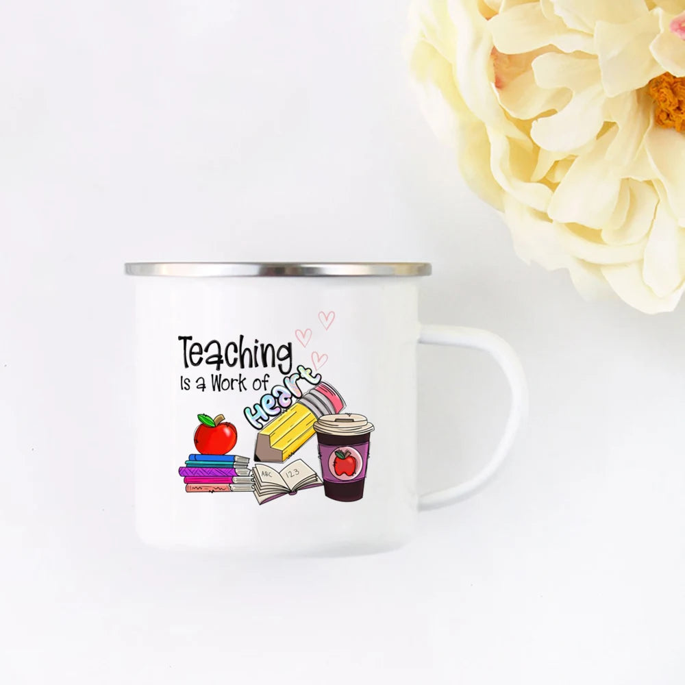 A white enamel mug featuring the text Teaching is a work of heart surrounded by small hearts and illustrations of an apple, a