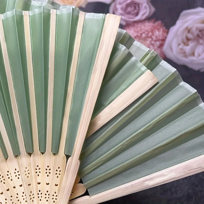 A set of light green and natural wood folding fans displayed on a dark surface.