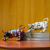 A white sculpture of a bull and a colorful, abstract animal sculpture are displayed on a wooden surface.