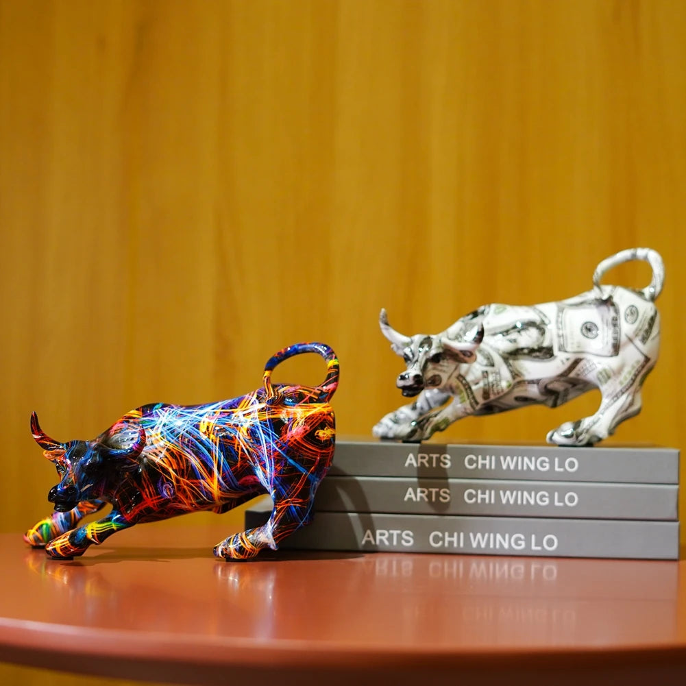 A white sculpture of a bull and a colorful, abstract animal sculpture are displayed on a wooden surface.