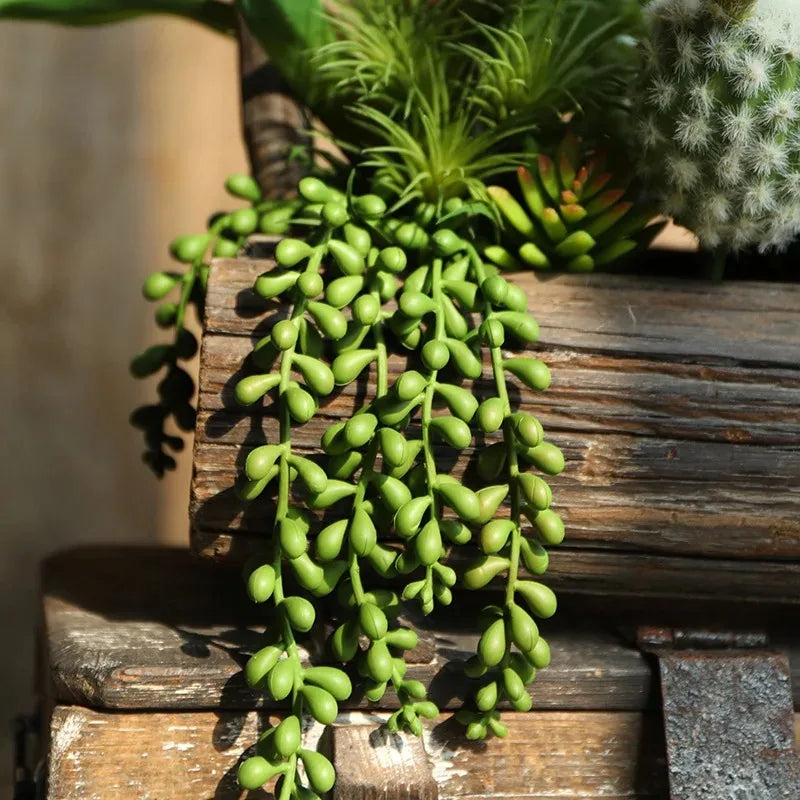 A vibrant green artificial hanging succulent vine with small leaves is displayed on a wooden surface.