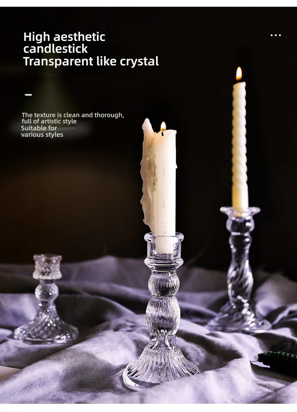 A tall, clear glass pillar candle holder with a white candle is displayed on a gray fabric.