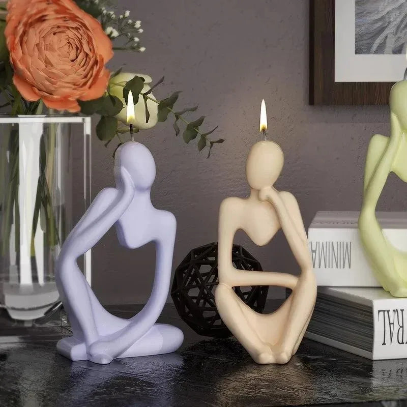 A pair of abstract silicone molds shaped like figures are displayed on a dark surface next to a vase of flowers.