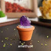 A purple amethyst crystal sits in an orange pot on a dark surface.