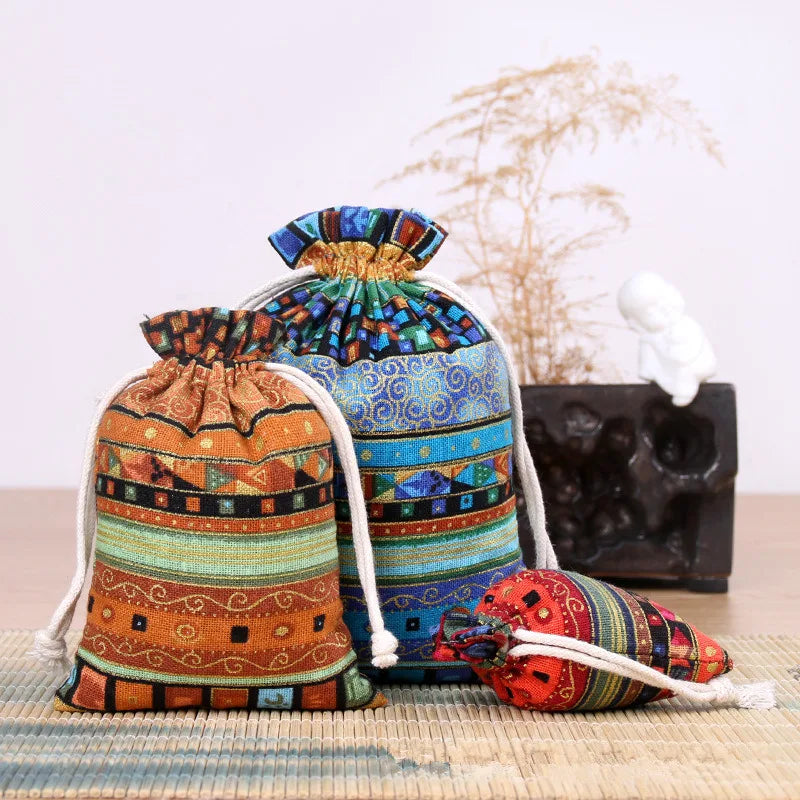 A set of vintage cotton drawstring gift pouches in various earthy and colorful patterns resting on a wooden surface.