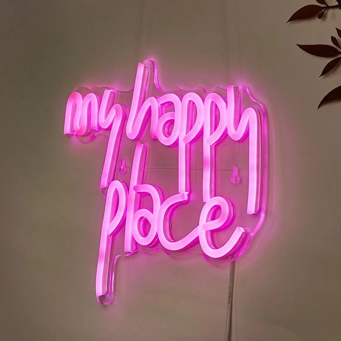 Pink LED neon sign spelling out My Happy Place mounted on a white wall.