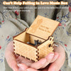 A hand holding a small wooden music box with a lid open, featuring an engraved design of a couple.