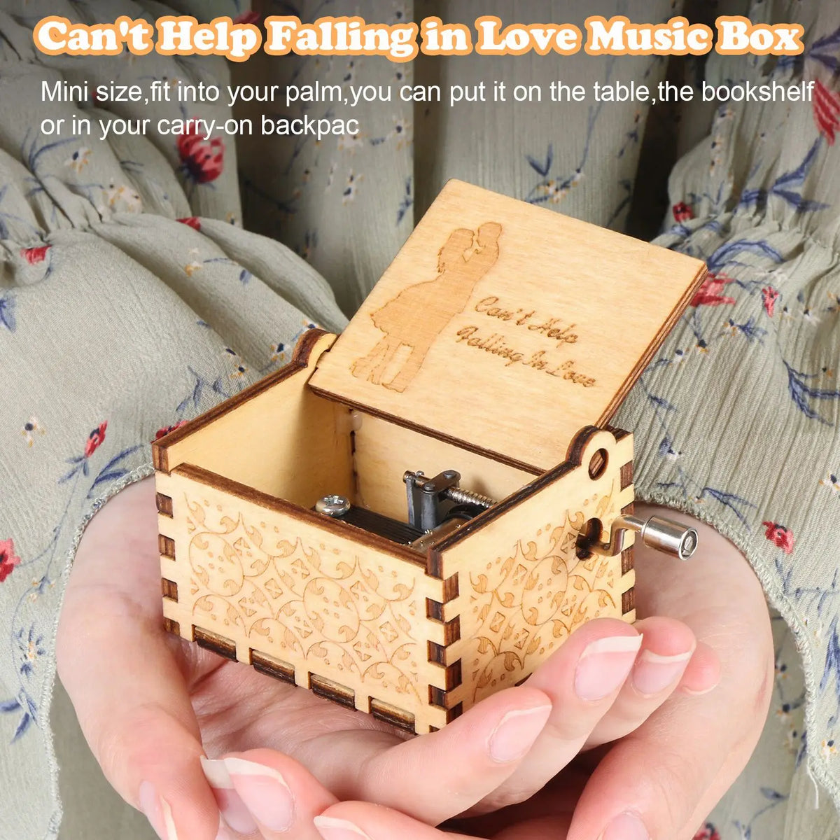 A hand holding a small wooden music box with a lid open, featuring an engraved design of a couple.
