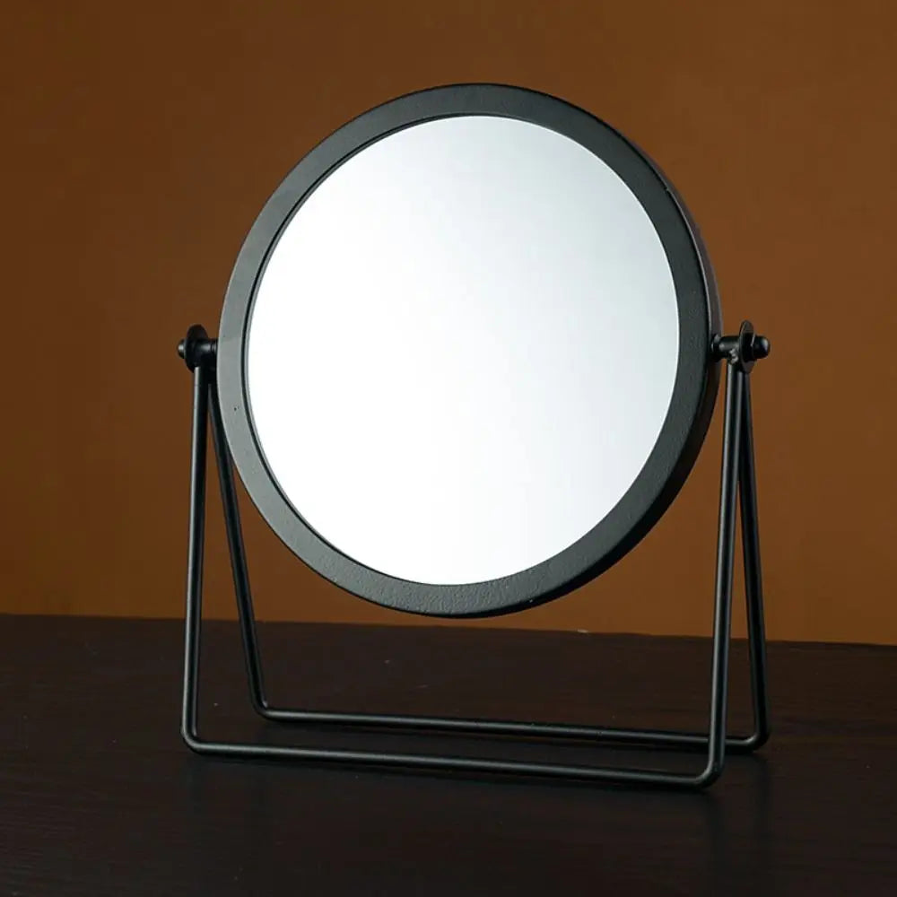 A round, black-framed makeup mirror with a rotating feature mounted on a metal stand.