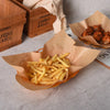 A pile of golden french fries served in a brown paper cone on a light surface.