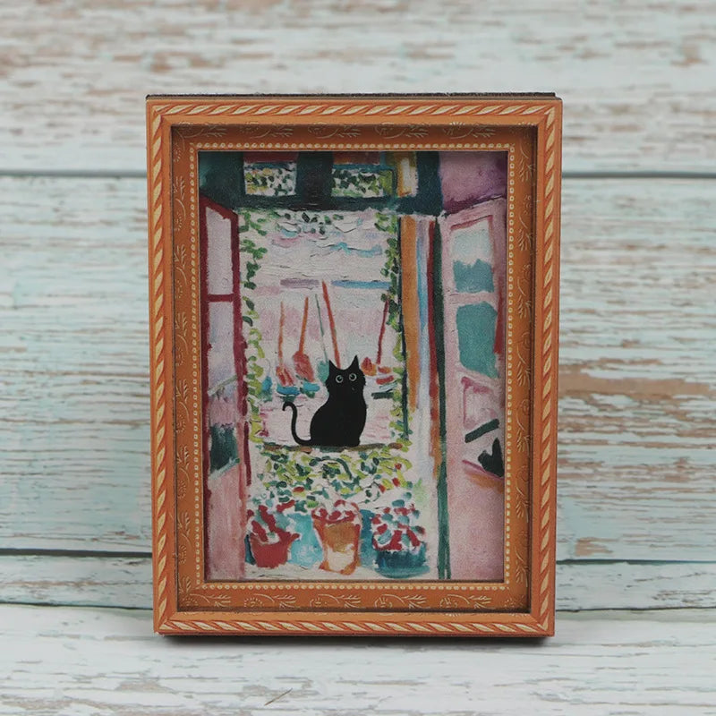 A framed painting featuring a black cat amidst greenery and pink tones, displayed in a wooden frame.