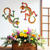 Handcrafted metal gecko wall art featuring colorful lizard figures displayed above a floral arrangement.