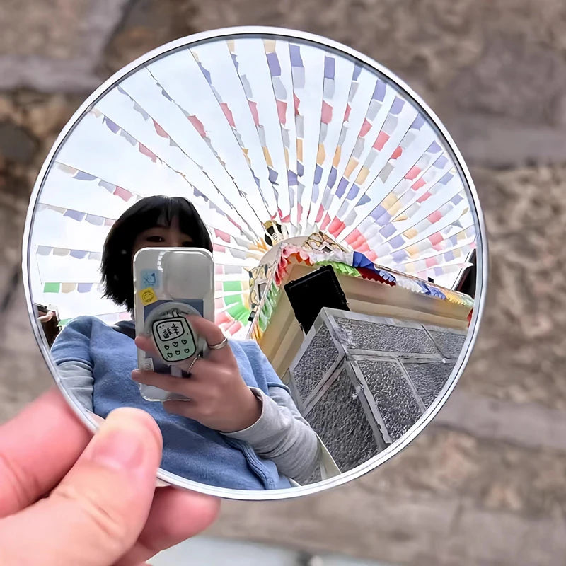 A hand holds a round convex mirror showing a colorful, striped reflection of the surroundings.