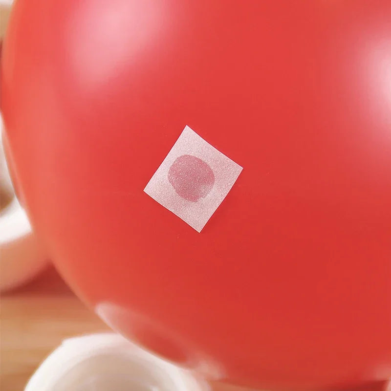 Primer plano de un globo rojo con una pequeña pegatina cuadrada y rosa adhesiva colocada en su superficie.