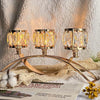 Three-arm gold crystal candelabra with three glass candle holders resting on a white fabric.