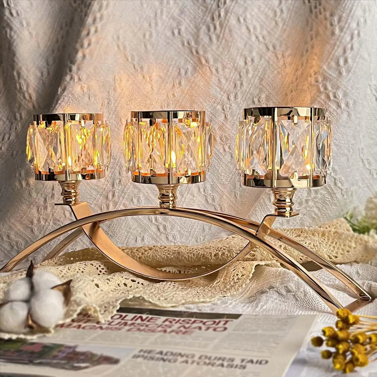 Three-arm gold crystal candelabra with three glass candle holders resting on a white fabric.