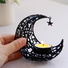 A hand holds a black, intricate crescent moon candle holder with a lit candle and a small star decoration.