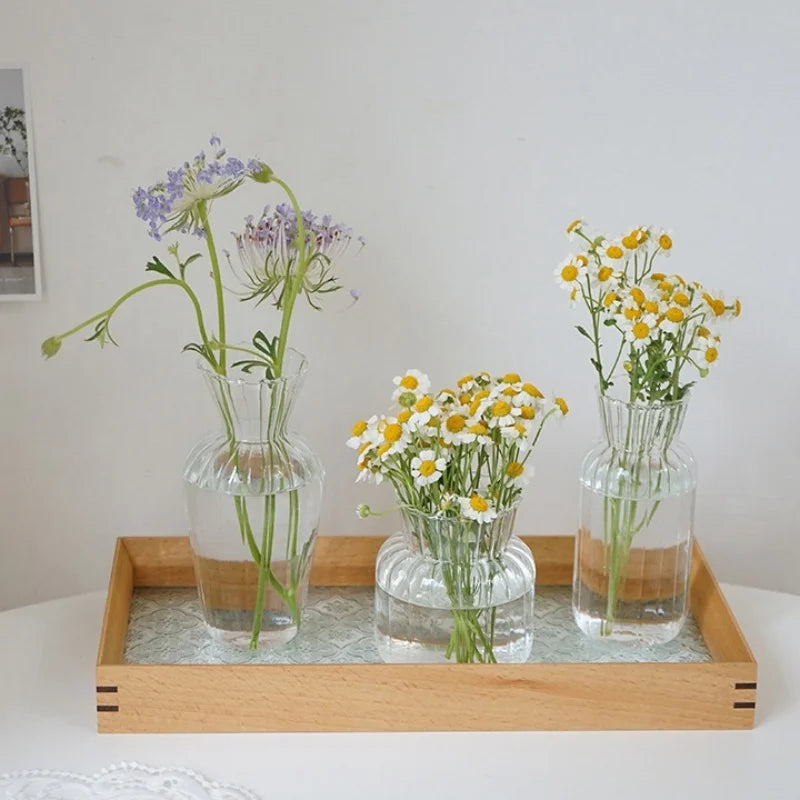 A wooden tray holds glass vases with purple and yellow wildflowers for home decor.
