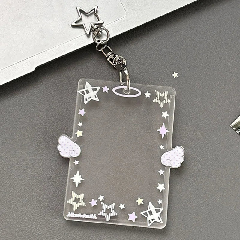 Clear acrylic photocard holder with stars and wings attached to a silver keychain.